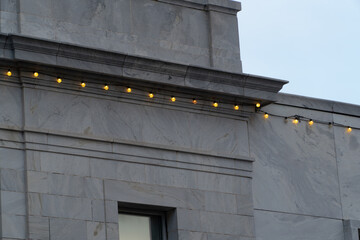 Elegant marble building facade adorned with warm glowing string lights against a clear evening sky, perfect for urban festive backgrounds and architectural design. © Michael