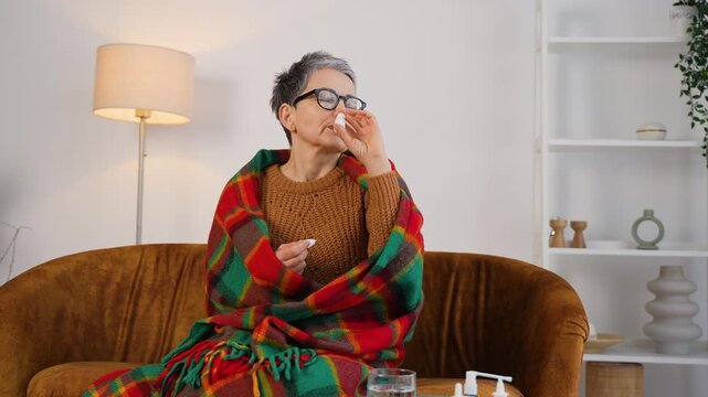 Sick older woman using nasal spray for flu and cold symptoms
