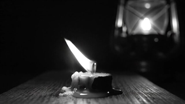 Candle flame flickering with smoke and a lamp on a wooden surface in complete darkness for a mysterious or spiritual ambiance.