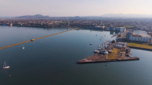 Panoramic coastal view of Granton Harbour and historical residential area in Edinburgh, Scotland, seen from the sea. The image features traditional stone architecture, sailing boat moorings, and old s
