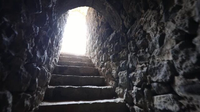  Moving slowly up a narrow, dark, and uneven stone staircase. The point of view approaches a bright arched exit, eventually stepping out into an overwhelmingly bright white light.