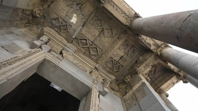 Low angle rotating view looking up at the beautifully carved stone ceiling and tall columns of an ancient classical structure, likely the historic Temple of Garni in Armenia.

