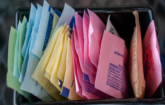 Assortment of vibrant artificial sweetener packets in a caddy, offering various sugar substitutes like Splenda, Sweet'n Low, and Stevia for coffee and tea, promoting a healthy, low-sugar lifestyle.
