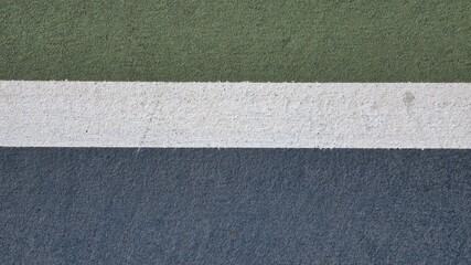 Fototapeta premium A top-down view of a textured sports court surface. Three horizontal bands of color—forest green, bright white, and deep blue—show a gritty, non-slip synthetic grain used for athletic play.