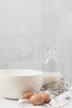 Eggs, Milk, Mixing Bowl and Whisk on Light Background