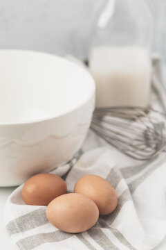 Eggs, Milk, Mixing Bowl and Whisk on Light Background