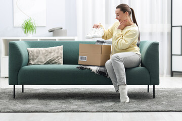 Fototapeta premium Excited woman taking sneakers from open parcel on sofa at home