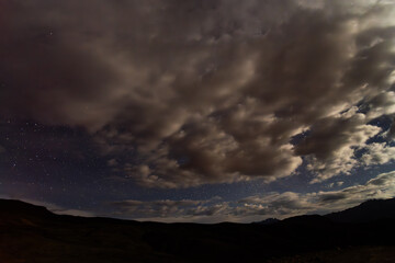 Fototapeta premium Starry night sky with clouds over mountain silhouette landscape