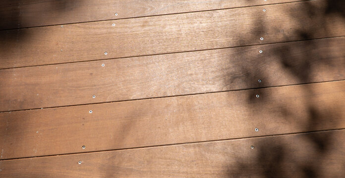 Warm natural wooden deck planks texture with sunlight and dappled shadows, ideal for outdoor background, flooring, construction, and rustic design elements.