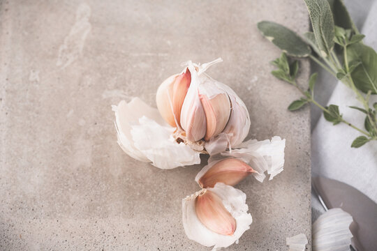 Head of Garlic Open on Cutting Board with Green Herbs and Knife Beside