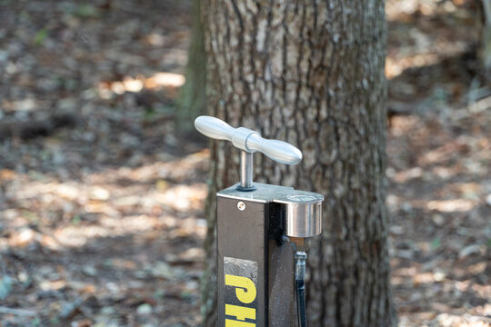 Outdoor public bicycle tire pump station, offering convenient air for cyclists on a scenic trail or park, with a natural blurred tree background.