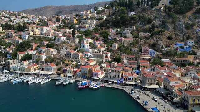Aerial panorama of colorful neoclassical houses and luxury yachts in Symi harbor, Greece. Picturesque Dodecanese island coastline at sunny day, 4K drone footage Part 2