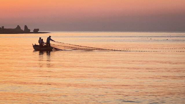 Fisherman casting net at sunrise on calm sea, golden morning light