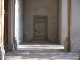 Obraz premium Aged wooden door set in a worn plaster wall with peeling paint. Minimal composition with soft natural light, highlighting texture, decay and timeless rustic character.