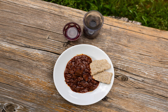 Wild game goulash boar deer venison with polenta on white plate rustic alpine outdoor table red wine