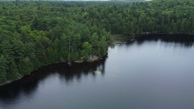 Flying over Buckskin Lake towards an old hunting lodge on an overcast, late summer afternoon. Aerial above the expansive crown land wilderness, located in Tory Hill, Highlands East, Ontario, Canada.