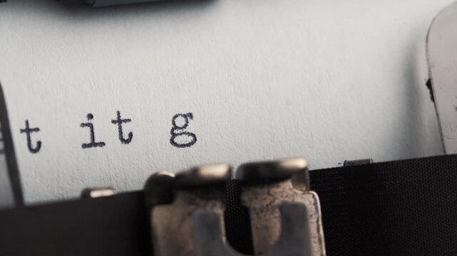 Writing LET IT GO on a typewriter with letters being printed on a sheet of paper in a close-up view showing the keys and mechanism