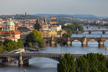 Obraz premium Aerial view of historic Prague showcasing the Vltava River, iconic bridges, and colorful architecture under a clear blue sky in the Czech Republic