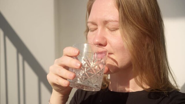 Woman enjoys drink while standing in sunlight, providing a moment of relaxation on a warm day