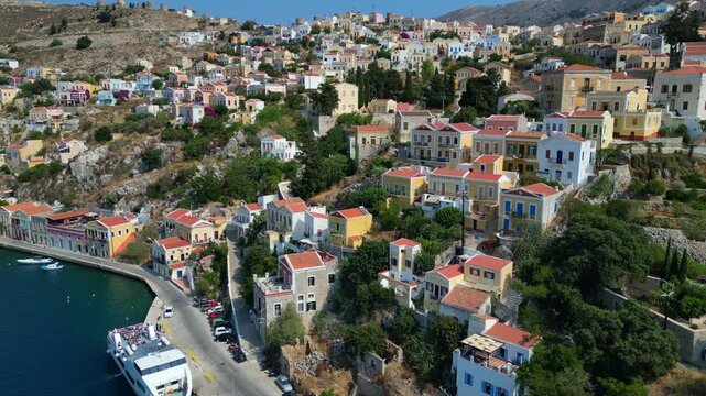 Aerial panorama of colorful neoclassical houses and luxury yachts in Symi harbor, Greece. Picturesque Dodecanese island coastline at sunny day, 4K drone footage