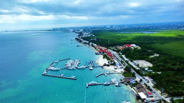 4K aerial drone view of a marina north of Puerto Juarez, Cancun. High-angle shot of luxury yachts and catamarans in turquoise water with a backdrop of lush mangroves and city horizon.