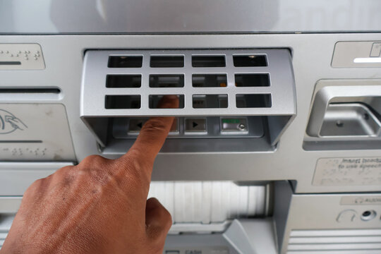 ​A person's hand typing a PIN code on an ATM machine keypad at a bank to authorize a secure financial transaction and access banking services safely.