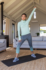 Asian woman stretching on black mat in modern living room near wood stove wearing mint top