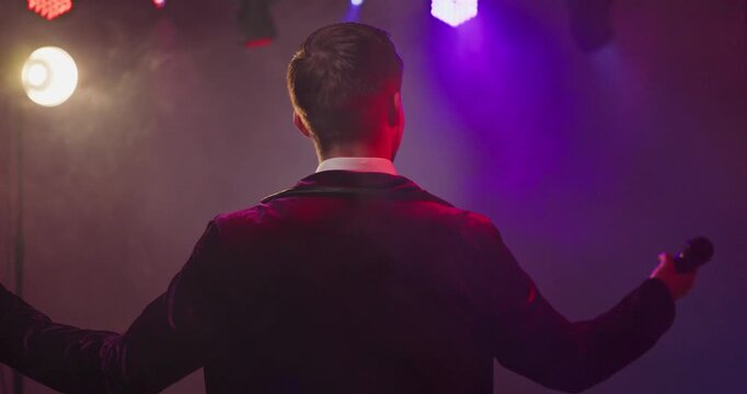 Presenter host showman speaking with microphone on stage. Announcer and performer addresses audience under lights and fog, ideal for promos and nightlife ads. Show hosting concept for ads.