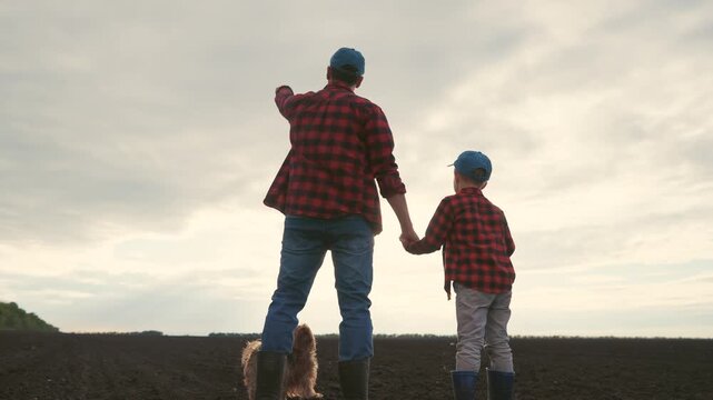 Father and son in a field. Silhouette of farmers and their son plowing a field. Family holding their father lifestyle sons hand. A dad and his son in a meadow.