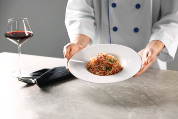 Professional chef with delicious pasta and red wine at grey marble table indoors, closeup