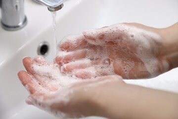 Fototapeta premium Woman washing hands with soap near white sink, closeup