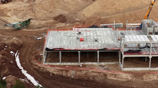 Ground-level view of a construction site with precast concrete beams, machinery, and building structure under development, highlighting industrial workflow and infrastructure progress.