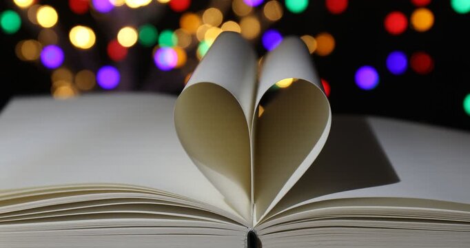 Heart made of book pages on table against blurred lights, closeup. Bokeh effect
