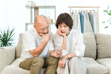 Fototapeta premium An elderly Asian couple using smartphone apps (confusing, confused, finding it difficult, feeling anxious)