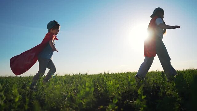 Two children running through field. Children playing superhero in a cape. A field of sunlight with a bunch of boys playing in it. Two kids sprinting across a meadow lifestyle.