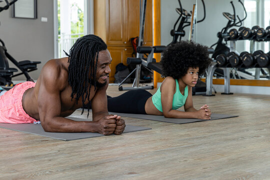 African father and teen daughter holding planks side by side on gym mats, smiling and working out together, showing African ethnicity, family bonding, and cross‑generational fitness motivation.