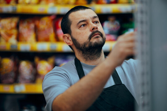 Supermarket Employee Arranging Merchandise on Shelves at Store. Grocery store clerk restock with products and check their placement on the shelf
