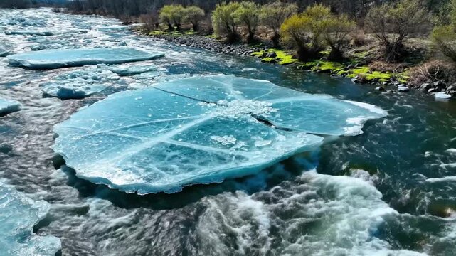 Aerial view of glacial ice pieces floating downstream through a rushing river with green banks