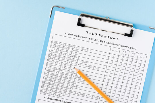 水色背景にバインダーに挟んだストレスチェックシートと鉛筆