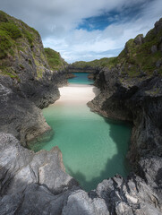Fototapeta premium A serene turquoise lagoon surrounded by rugged cliffs and rocky shores under a partly cloudy sky
