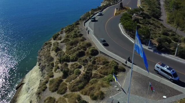 Aerial shot of the boardwalk curve in the city of Puerto Madryn Chubut. The drone shows the sea hitting cliffs and the tourist flow near the ACA camping.