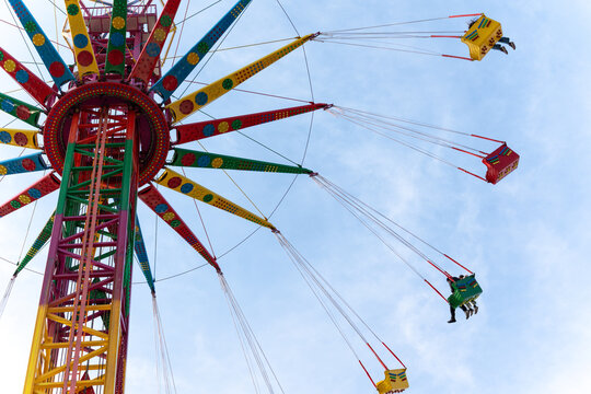 A low-angle shot of a vibrant, colorful swing ride in motion against a bright blue sky. People are enjoying the thrilling amusement park attraction.