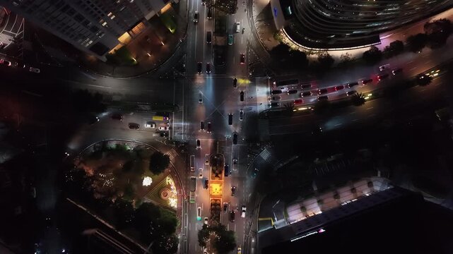 Night bird eye drone view of a major urban intersection in Makati City with pedestrian crossings and a warm-lit circular plaza surrounded by dark buildings and converging multi-lane roads below