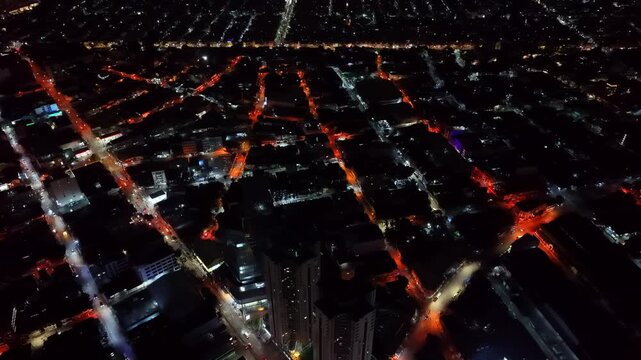 Very high altitude night aerial rotating slowly above a dense metropolitan grid where amber-lit streets form an abstract circuit board pattern between dark low-rise building blocks in Metro Manila