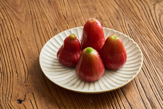 Four Red Wax Apples on a Vintage Fluted Ceramic Plate over a Natural Wood Grain Table