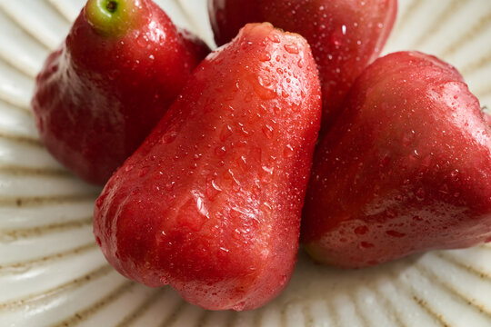 Four Red Wax Apples on a Vintage Fluted Ceramic Plate over a Natural Wood Grain Table