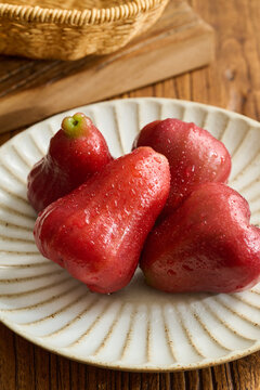 Four Red Wax Apples on a Vintage Fluted Ceramic Plate over a Natural Wood Grain Table