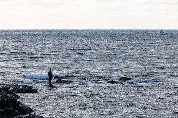 Obraz premium idyllic seascape with a man fishing on the rocky shore in Jeju Island, South Korea