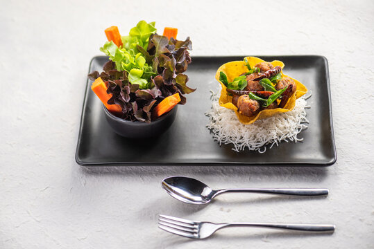 A delicious and colorful meal with a crispy shell filled with stir-fried vegetables and meat, served with a side salad.