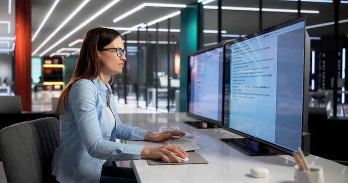 Woman Diligently Proofreads Document On Desktop Monitor